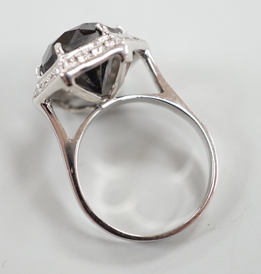 A modern 750 white metal and hexagonal cut black diamond set dress ring, with diamond chip set border, size N/O, gross weight 7.8 grams.